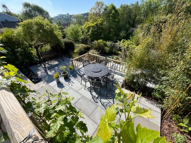 An outdoor patio with a round metal table and chairs surrounded by plants and trees at Old Orchard in Saundersfoot