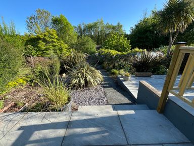 A garden with various plants and a stone path viewed from a patio at Old Orchard in Saundersfoot