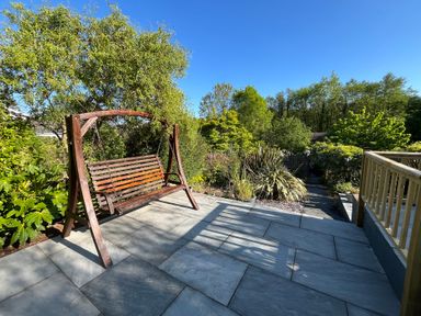 A wooden garden swing on a stone patio beside plants and trees at Old Orchard in Saundersfoot
