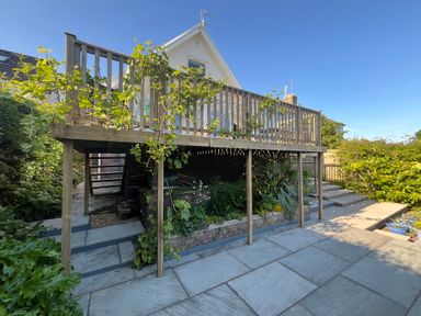 An outdoor patio with stone tiles and a wooden deck with railing and plants at Old Orchard in Saundersfoot