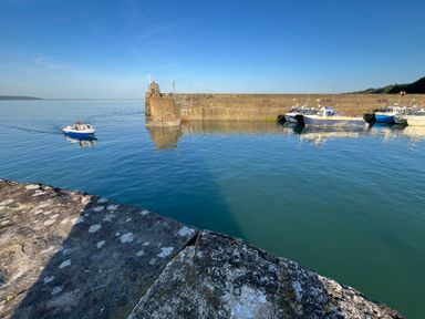 A small boat on water near a stone pier with other boats docked at Old Orchard in Saundersfoot