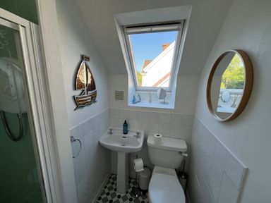 A small bathroom with a toilet sink round mirror a sailboat wall decoration and a window at Old Orchard in Saundersfoot