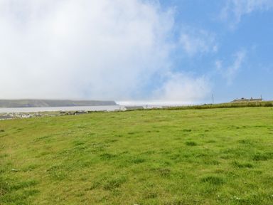 A grassy field with houses at a distance under a cloudy sky at 13 Trawmore Cottages in Keel County Mayo