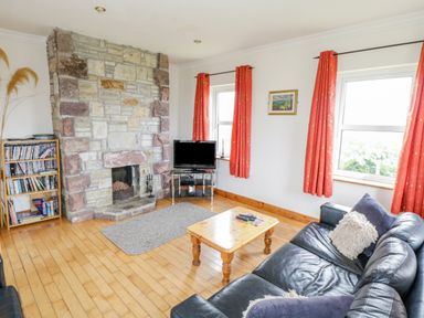 A living room with a stone fireplace a wooden coffee table a black leather sofa and two windows with red curtains at 13 Trawmore Cottages in Keel County Mayo