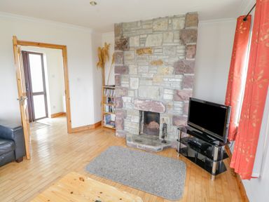 A living room with a stone fireplace a TV on a stand a grey rug and red curtains at 13 Trawmore Cottages Keel County Mayo