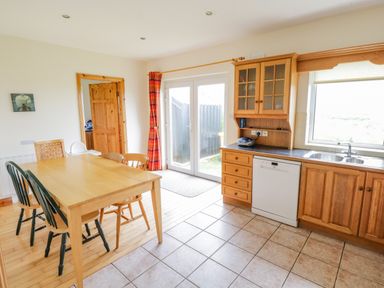 A kitchen and dining area with wooden cabinets a dining table with chairs and glass doors at 13 Trawmore Cottages Keel County Mayo