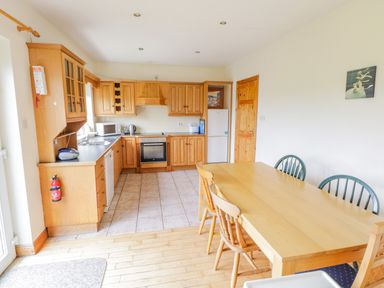 A kitchen with wooden cabinets tiled floor and a wooden dining table with chairs at 13 Trawmore Cottages Keel County Mayo