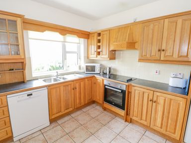 A kitchen with wooden cabinets a dishwasher an oven a microwave a toaster and a sink under a window at 13 Trawmore Cottages in Keel County Mayo