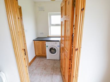 A laundry room with a washing machine under a countertop next to a wooden cabinet at 13 Trawmore Cottages in Keel County Mayo
