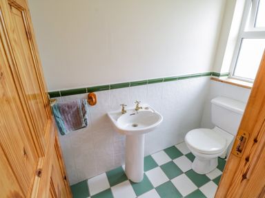 A bathroom with a white sink and toilet and green and white tiled floor at 13 Trawmore Cottages in Keel County Mayo