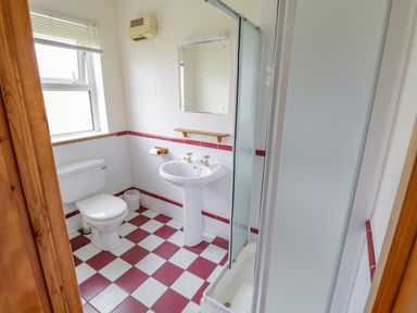 A bathroom with a toilet sink mirror and shower with red and white tiled floor at 13 Trawmore Cottages Keel County Mayo