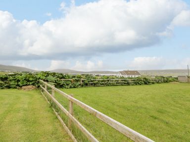 A fenced grassy field with plants and a house in the distance at 13 Trawmore Cottages in Keel County Mayo