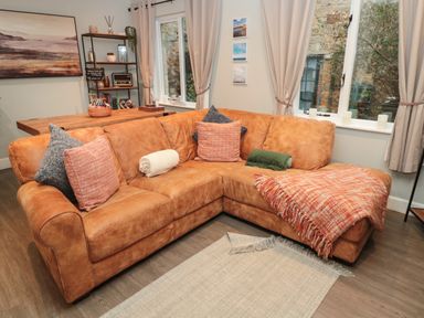 A living room with a brown leather corner sofa and a wooden dining table at Dodds Nook in Alnwick