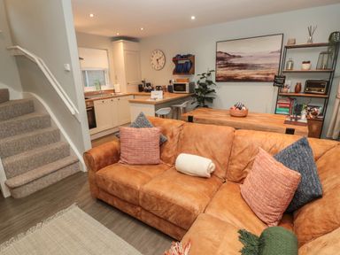A living room with a brown couch and a kitchen with white cabinets and a wooden counter at Dodds Nook in Alnwick