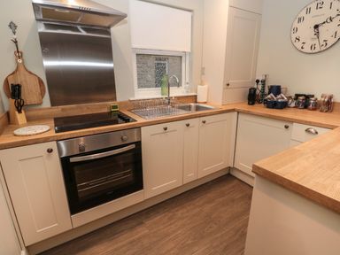 A kitchen with wooden countertops white cabinets a stove oven sink and a clock on the wall at Dodds Nook in Alnwick