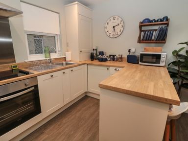 A kitchen with wooden countertops white cabinets a microwave a wall clock and dishes on a rack at Dodds Nook in Alnwick