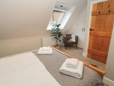 A bedroom with a wooden bed frame and folded towels on the bed near a leather chair and a plant by a skylight window at Dodds Nook in Alnwick