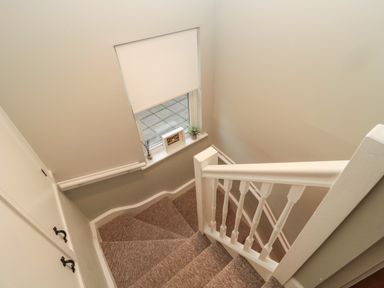 A carpeted staircase with a white banister and a window with a roller blind and small decorations on the sill at Dodds Nook in Alnwick