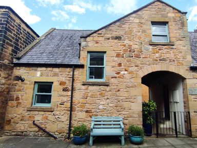 Stone building exterior with blue bench and two blue plant pots at Dodds Nook in Alnwick