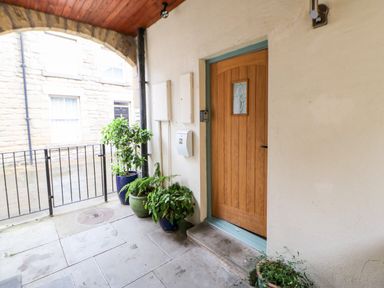 A covered outdoor entrance with a wooden door and several potted plants along the wall at Dodds Nook in Alnwick