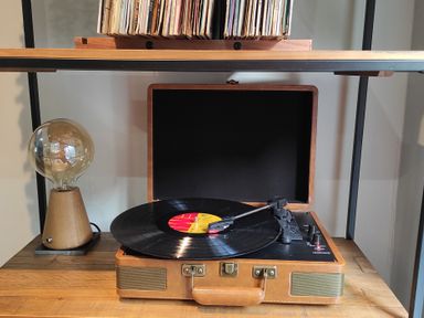 A record player with a vinyl record on a wooden table next to a lamp and a shelf with vinyl records at Dodds Nook in Alnwick