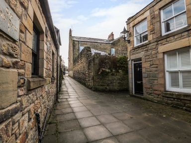 A narrow paved alleyway between stone buildings with windows and doors at Dodds Nook in Alnwick
