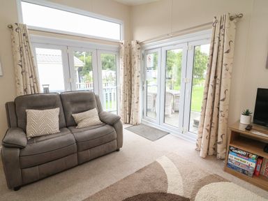 A living room with a sofa pillows board games and glass doors at Waterside Lodge South Lakeland Leisure Village near Carnforth