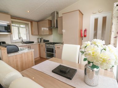 A kitchen and dining area with cabinets stove microwave and flowers on a table at Waterside Lodge South Lakeland Leisure Village near Carnforth