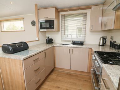 A kitchen with cabinets a microwave oven a gas stove a sink a bread box a toaster and a kettle at Waterside Lodge in South Lakeland Leisure Village near Carnforth