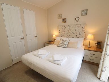 A bedroom with a double bed two bedside tables with lamps two closed doors on one wall and wall decorations at Waterside Lodge South Lakeland Leisure Village near Carnforth