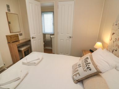 A bedroom with a bed a bedside table a lamp a vanity desk and an open door showing a bathroom at Waterside Lodge South Lakeland Leisure Village near Carnforth