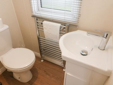 A bathroom with a toilet a sink a towel rail with a towel and a window at Waterside Lodge South Lakeland Leisure Village near Carnforth