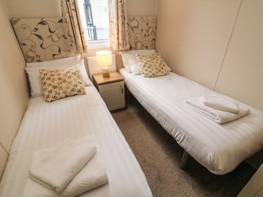 A bedroom with two single beds a bedside table with lamp and a window at Waterside Lodge South Lakeland Leisure Village near Carnforth