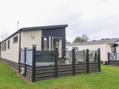 An outdoor deck with chairs and a hot tub next to a modular home at Waterside Lodge South Lakeland Leisure Village near Carnforth
