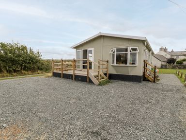 A single-story house with a gravel driveway and wooden porch railings at Porthwen Lodge in Bull Bay near Cemaes Bay
