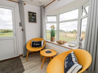 A small sitting area with two yellow chairs and a round table near windows with curtains at Porthwen Lodge in Bull Bay near Cemaes Bay
