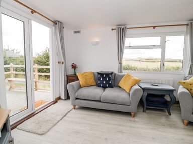 A living room with grey sofas yellow and blue cushions a blue side table and sliding glass doors at Porthwen Lodge in Bull Bay near Cemaes Bay