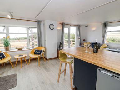 A living area with wooden floor yellow chairs round table a bar counter with stools and a sofa at Porthwen Lodge Bull Bay near Cemaes Bay
