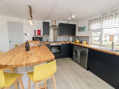 A kitchen with wooden countertops yellow chairs and black cabinets at Porthwen Lodge in Bull Bay near Cemaes Bay