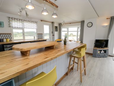 A kitchen area with wooden countertops yellow chairs windows and a small television on a stand at Porthwen Lodge in Bull Bay near Cemaes Bay
