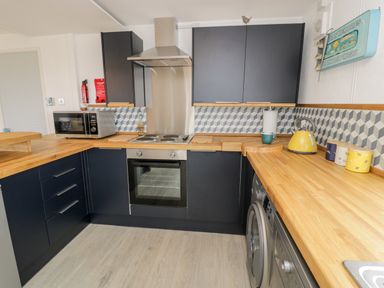 A kitchen with dark cabinets wooden countertops microwave oven stove and washing machine at Porthwen Lodge Bull Bay near Cemaes Bay