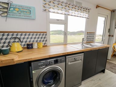 A kitchen counter with a washing machine dishwasher sink and window at Porthwen Lodge in Bull Bay near Cemaes Bay