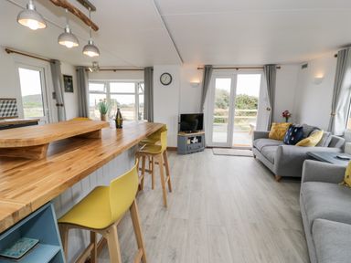 A living room with sofas yellow chairs and a wooden counter at Porthwen Lodge Bull Bay near Cemaes Bay