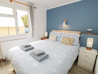 A bedroom with a bed featuring blue and white bird-patterned bedding two bedside tables with lamps and folded towels on the bed at Porthwen Lodge Bull Bay near Cemaes Bay