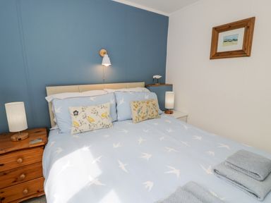 A bedroom with a bed with bird patterned bedding and cushions with nightstands and lamps at Porthwen Lodge in Bull Bay near Cemaes Bay