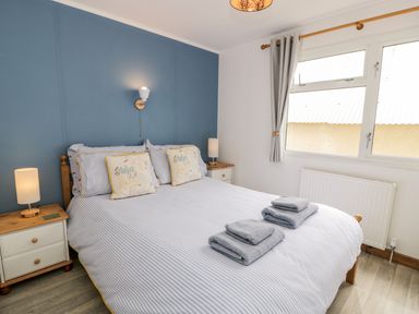 A bedroom with a double bed with striped bedding two bedside tables with lamps and a window with curtains at Porthwen Lodge Bull Bay near Cemaes Bay