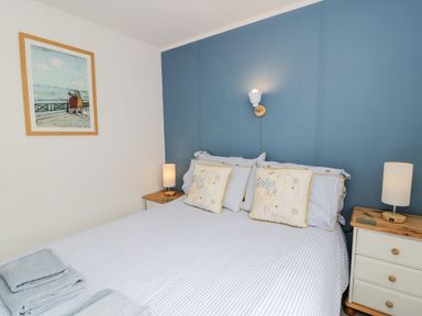 A bedroom with a bed with pillows and towels bedside tables with lamps and a painting on the wall at Porthwen Lodge in Bull Bay near Cemaes Bay