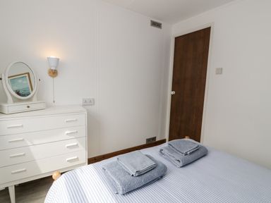 A bedroom with a bed with folded towels a white dresser with a mirror and a wall light at Porthwen Lodge in Bull Bay near Cemaes Bay