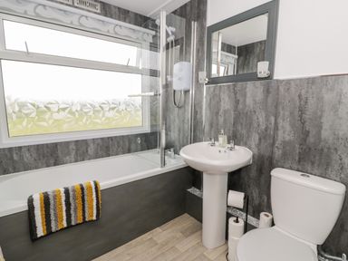 A bathroom with a bathtub towel sink toilet and mirror at Porthwen Lodge in Bull Bay near Cemaes Bay