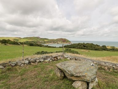 A grassy hillside with a stone table and low stone fence overlooking fields sea and a distant hill at Porthwen Lodge in Bull Bay near Cemaes Bay
